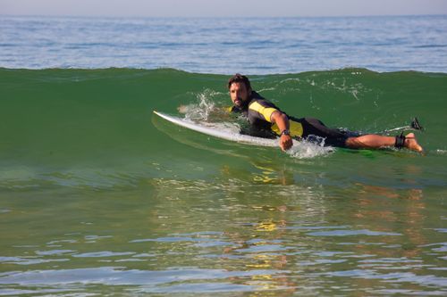 Free Side view full body energetic male surfer in wetsuit lying on surfboard on seawater and looking at camera Stock Photo