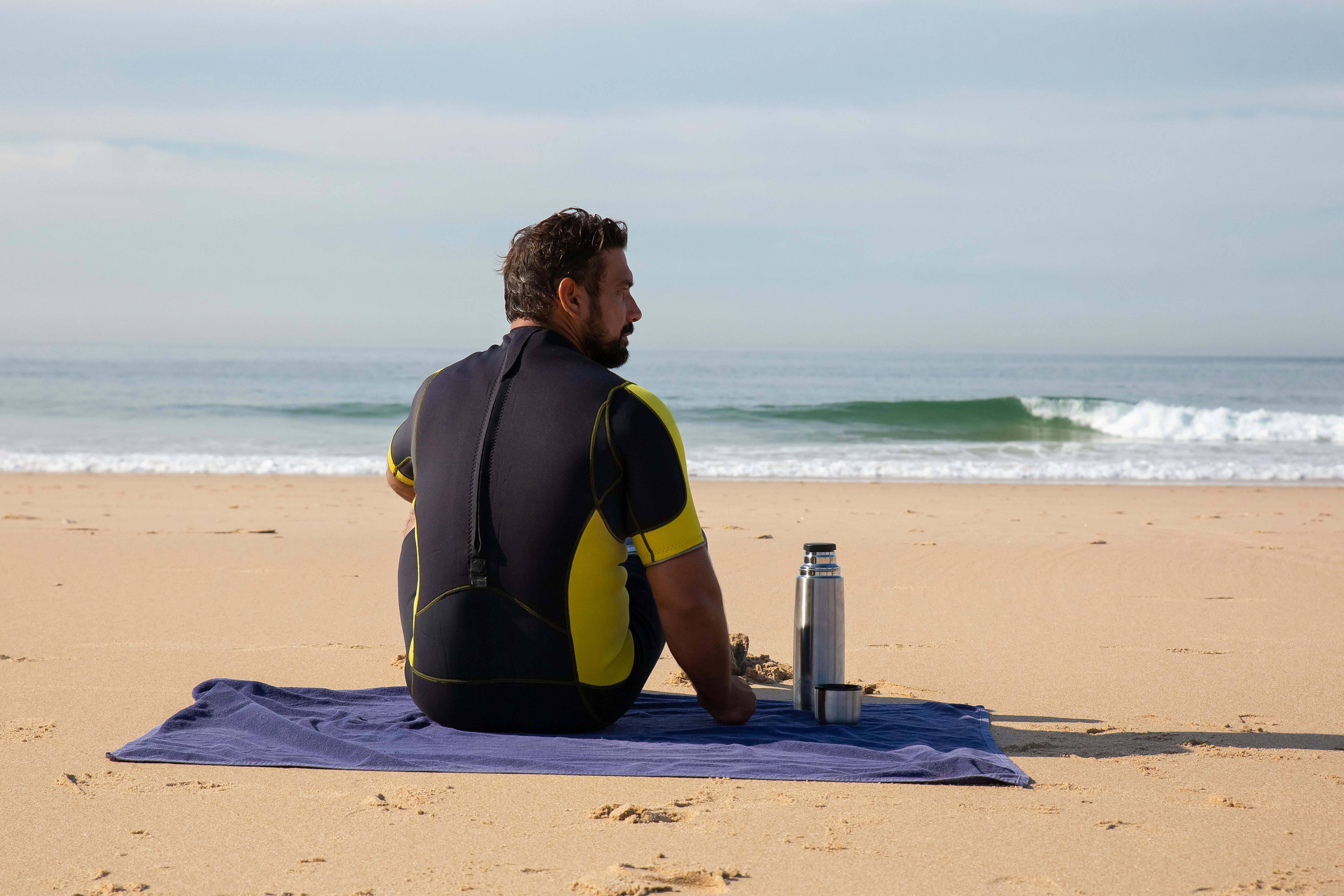 male surfer resting on seacoast with thermos