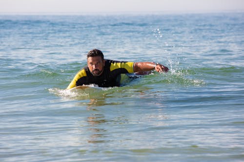 Free Dedicated ethnic male surfer floating on surfboard on seawater Stock Photo
