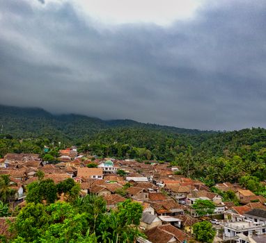 Picturesque drone view of small settlement with typical red roofed houses surrounded by lush green vegetation under overcast sky - Fotografer Sidoarjo