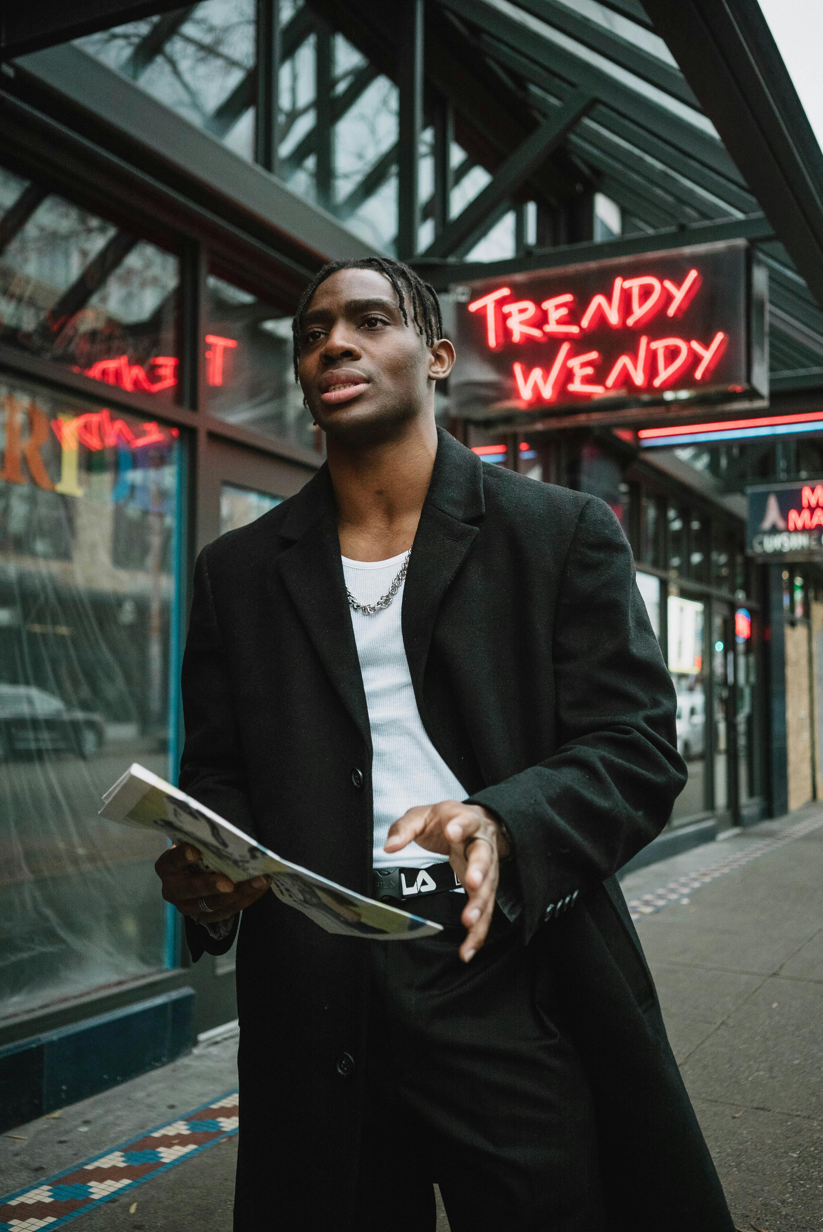 serious young ethnic guy standing on street with newspaper in hand