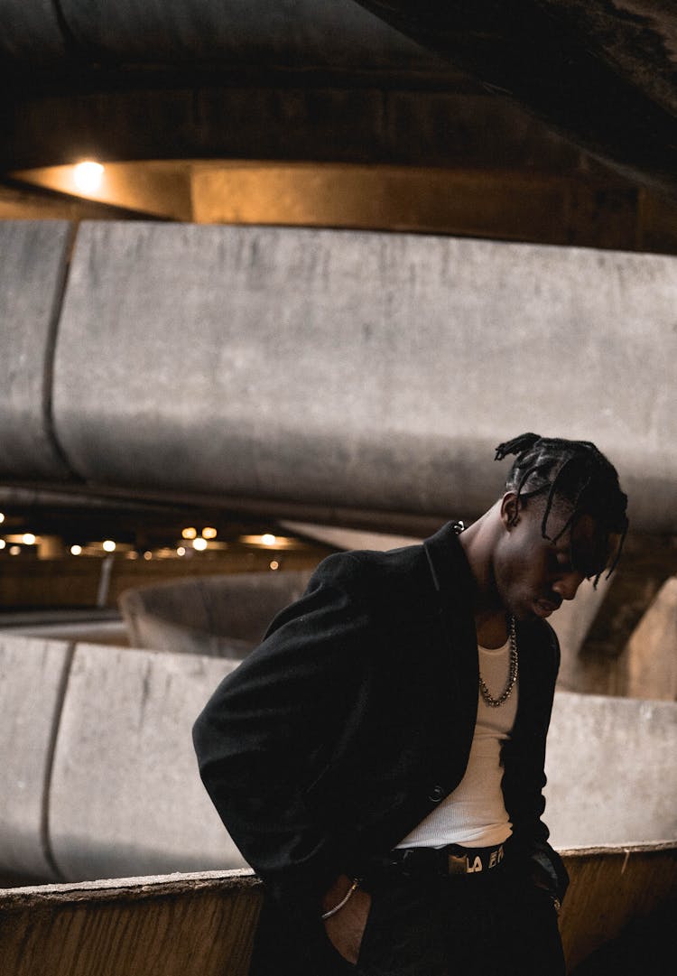 Serious Young Black Guy Relaxing In Multilevel Indoor Parking Building And Looking Down Thoughtfully