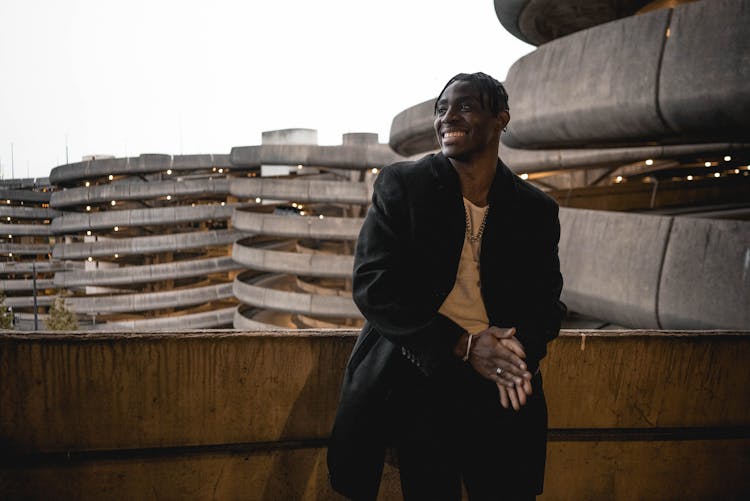 Happy Black Man Smiling With Hands Together In Concrete Balcony