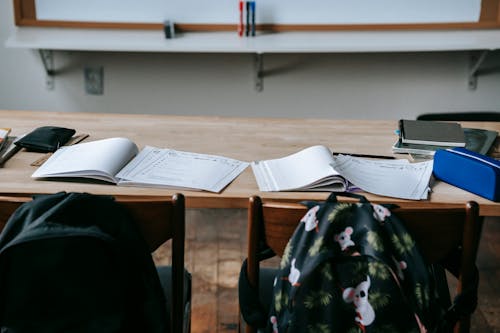 School desk with opened textbooks and stationery against whiteboard in modern light classroom