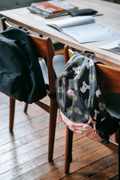 School desk with opened copybooks textbooks and stationery near chairs with backpack in light modern classroom