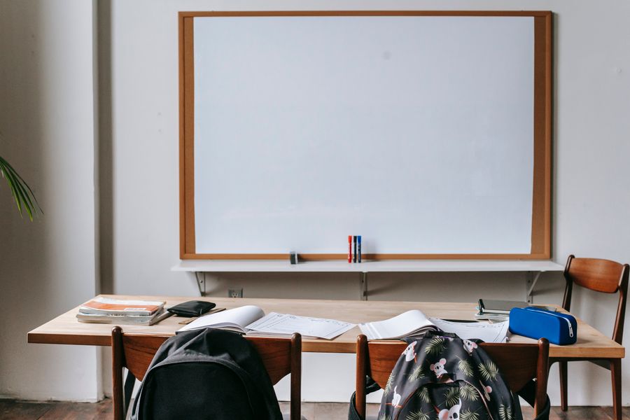Classroom with whiteboard and wooden desks holding open books and stationery