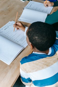 From above concentrated African American pupils sitting at desk and writing in notebooks during class in school