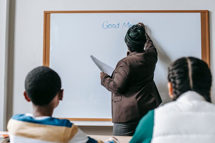 A teacher writing on a whiteboard with two pupils seen from behind
