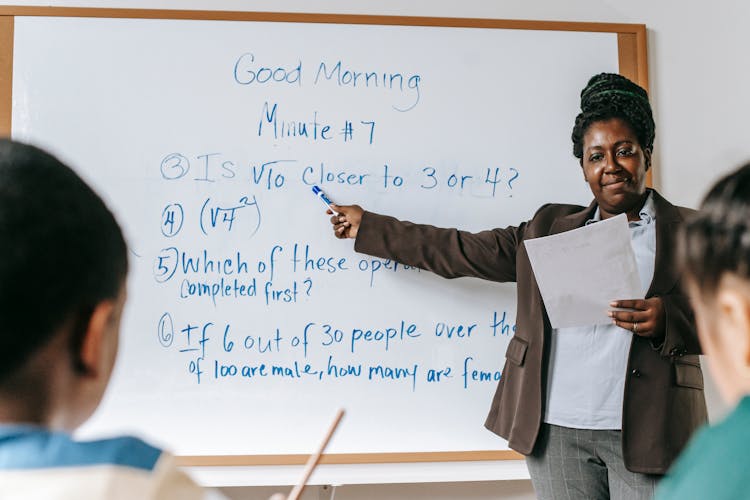 Positive Black Teacher Pointing At Tasks On Whiteboard