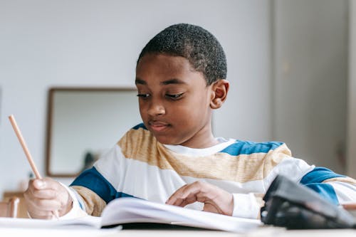 Positive black boy doing homework in copybook