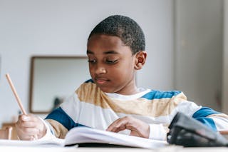 Positive black boy doing homework in copybook