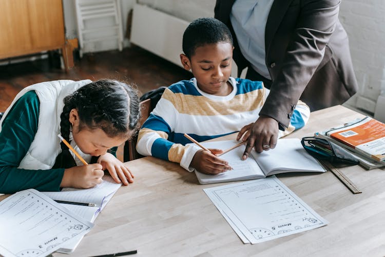 Anonymous Ethnic Tutor Helping Little Multiracial Students With Task In Classroom