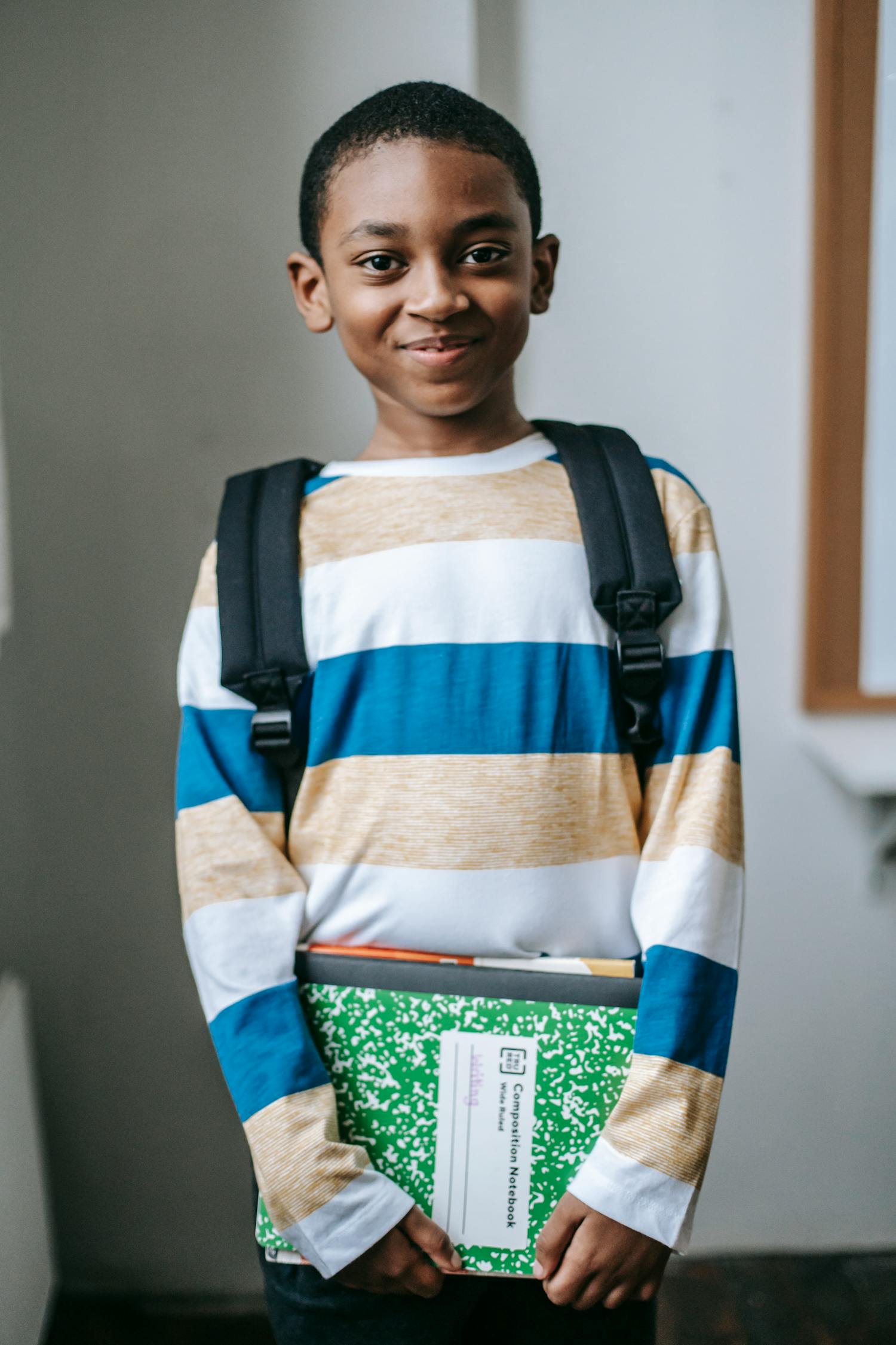 Cheerful schoolboy holding books and smiling in a classroom setting, ready for learning.