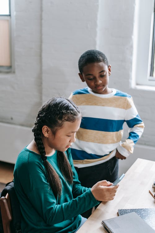Free Adorable multiracial little friends browsing smartphone during break in classroom Stock Photo