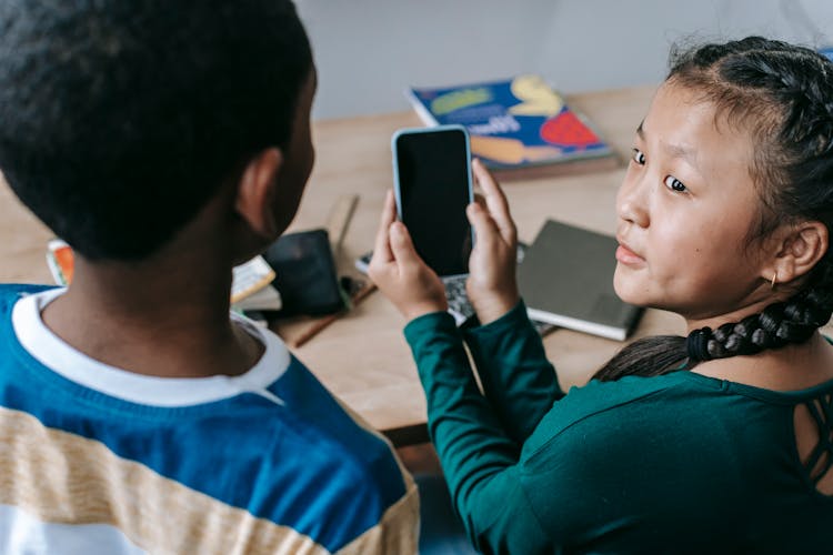 Cute Diverse Schoolchildren Sharing Smartphone During Break In Classroom