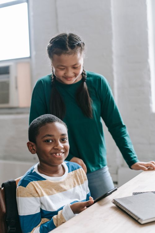 Free Positive Asian schoolgirl in casual clothes with long dark hair standing near smiling African American friend watching video on smartphone in classroom Stock Photo
