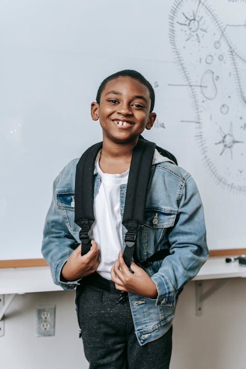 Cheerful black kid standing near whiteboard in classroom