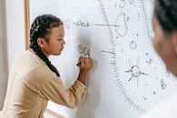 Side view of ethnic schoolgirl holding marker pen and writing on whiteboard during biology lesson in school