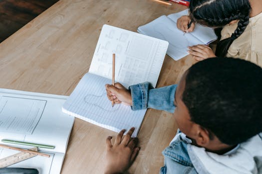 From above of crop unrecognizable students in casual clothes sitting at desk with copybook and doing exercise in classroom