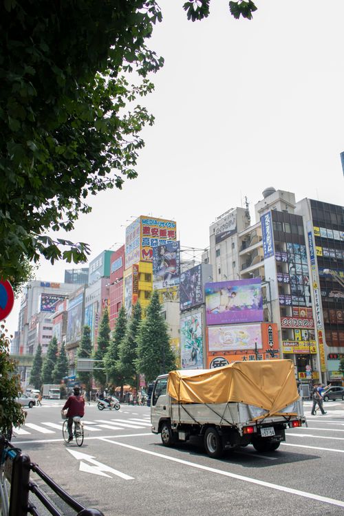 Free Vibrant city street in Chiyoda City, Tokyo with vehicles, cyclists, and colorful high-rises. Stock Photo