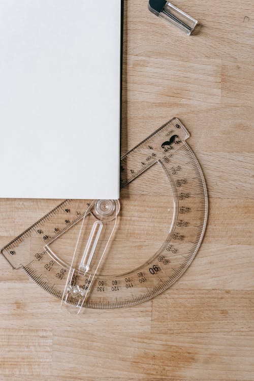 Composition of protractor under white sheet of paper on wooden table in school