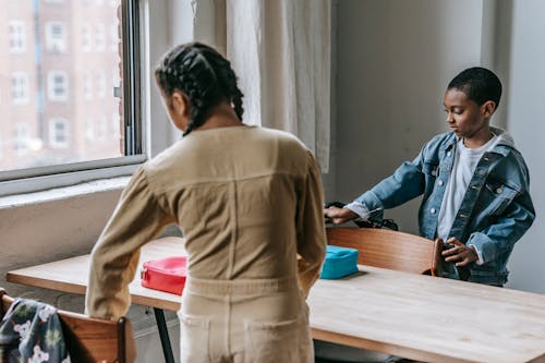 Multiracial classmates gathering at table with lunch boxes and preparing for breakfast together