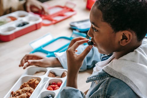 Crop black boy eating blueberries in school