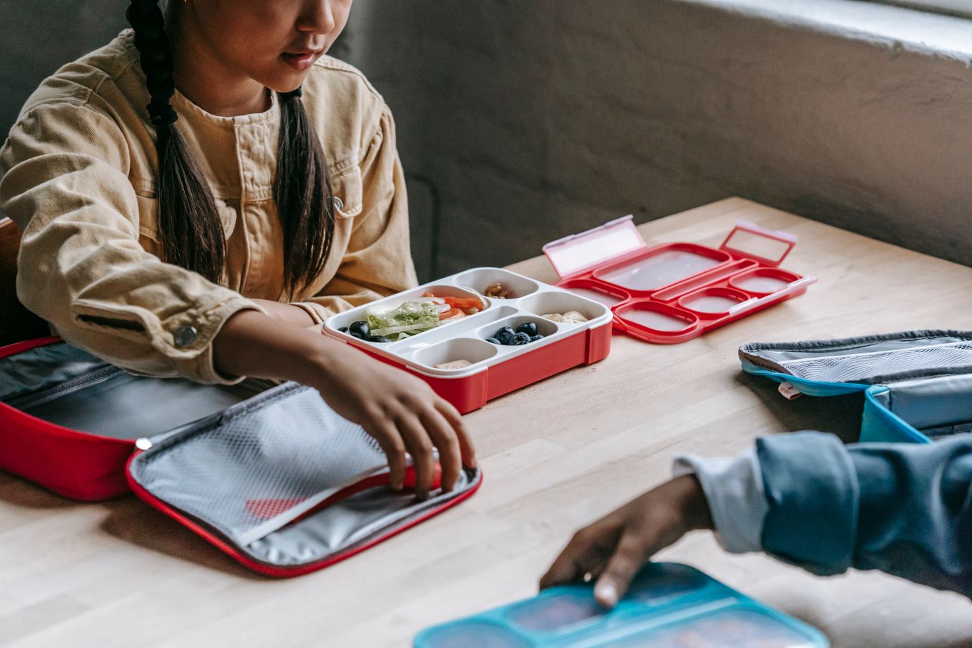 School-aged children unpacking reusable lunch boxes at a table