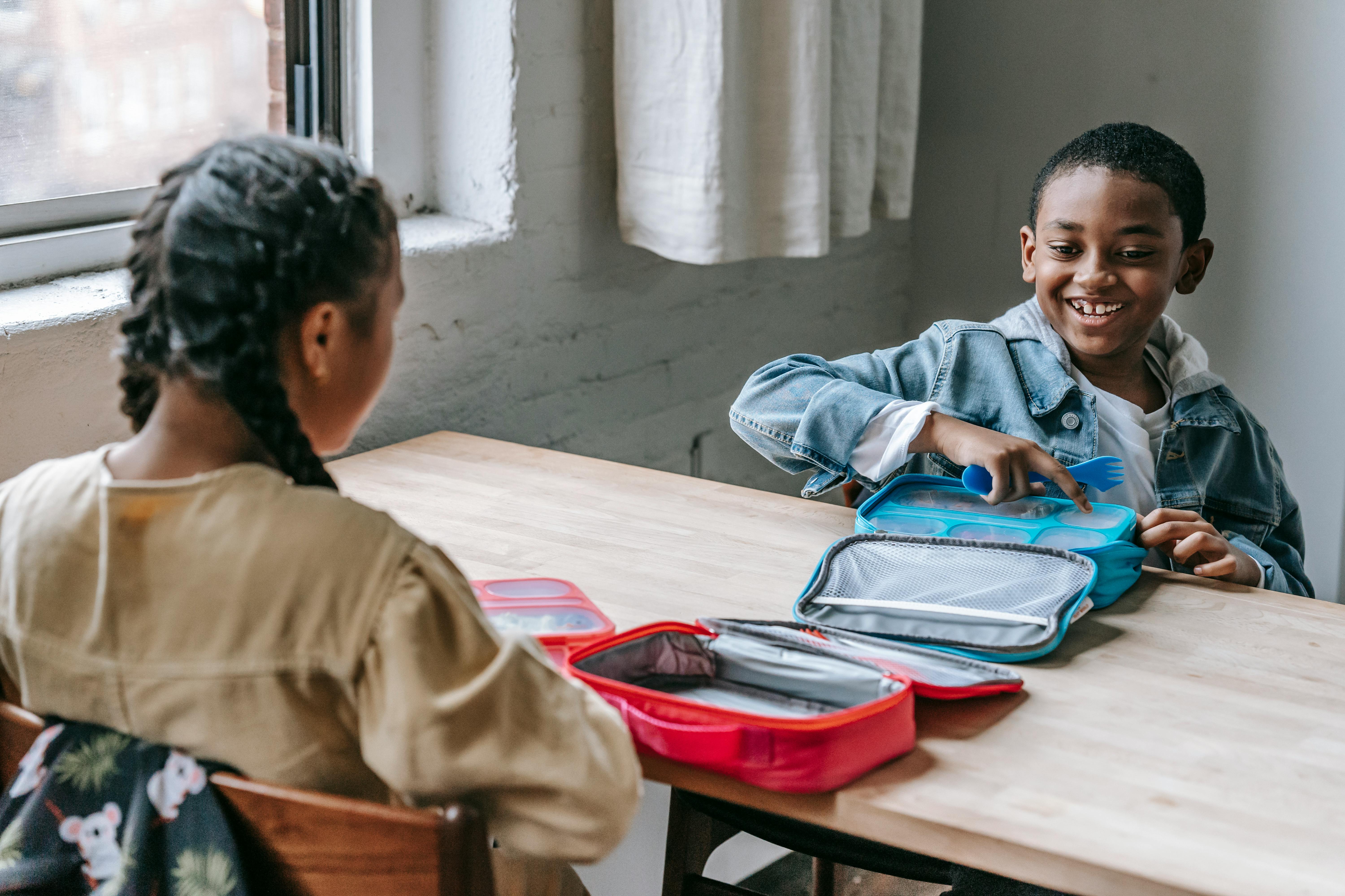 cheerful black schoolboy with lunch box against unrecognizable girl