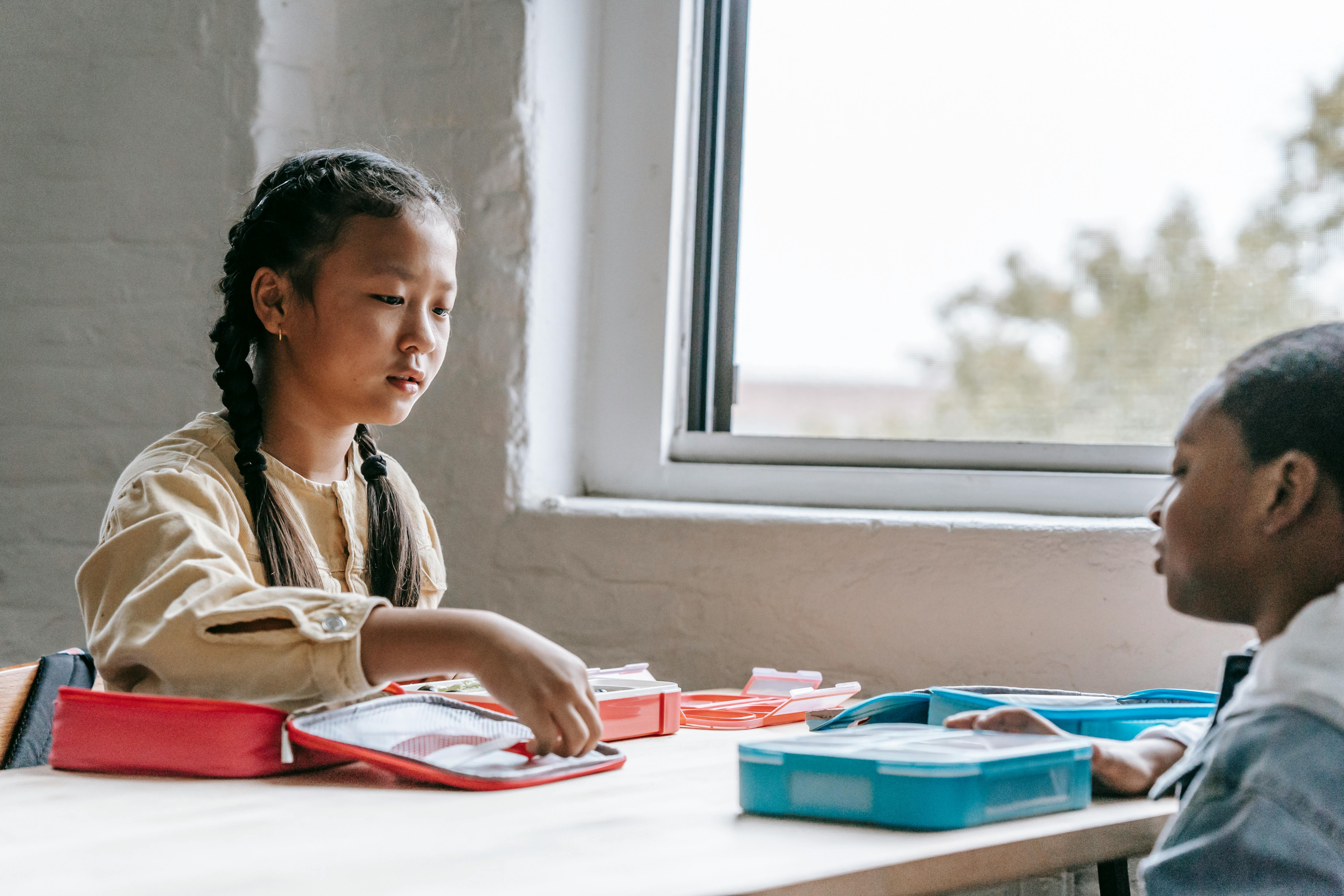 crop multiethnic schoolchildren with lunch boxes near window