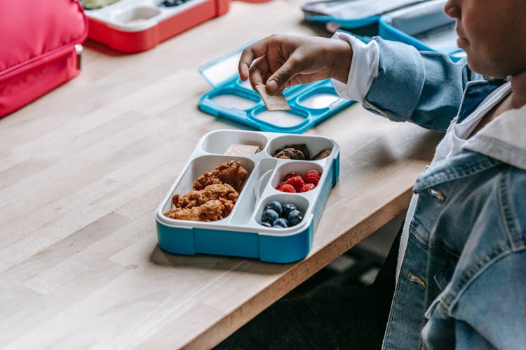 Crop Black Schoolchild With Biscuit Near Lunch Box