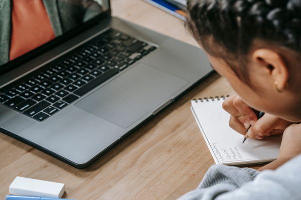 Student studying online with a laptop while writing notes