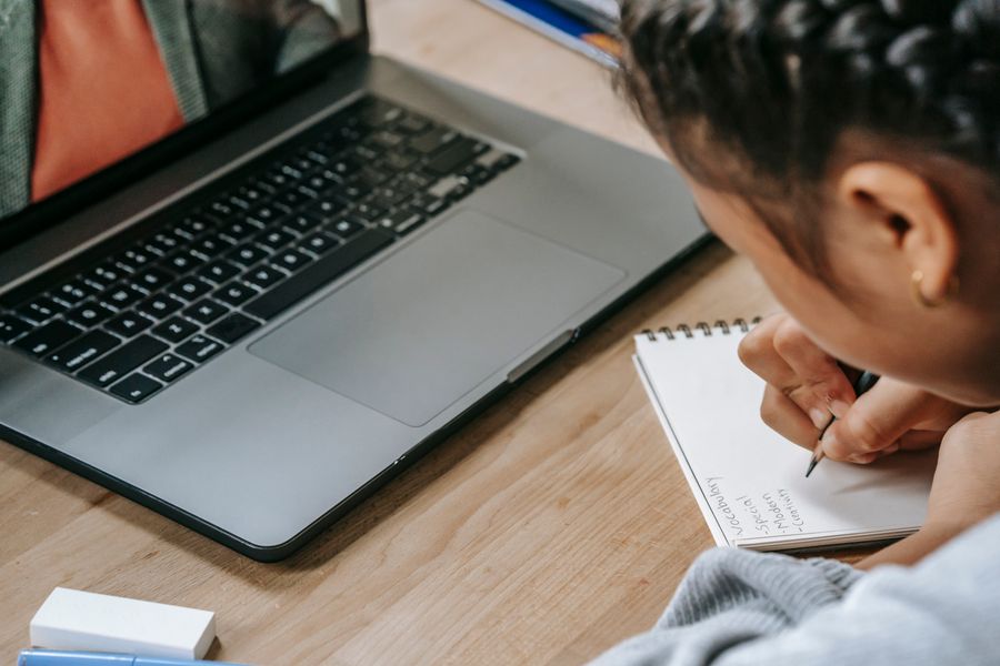 Student studying online with a laptop while writing notes