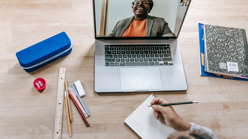 Person writing notes beside a laptop during an online session