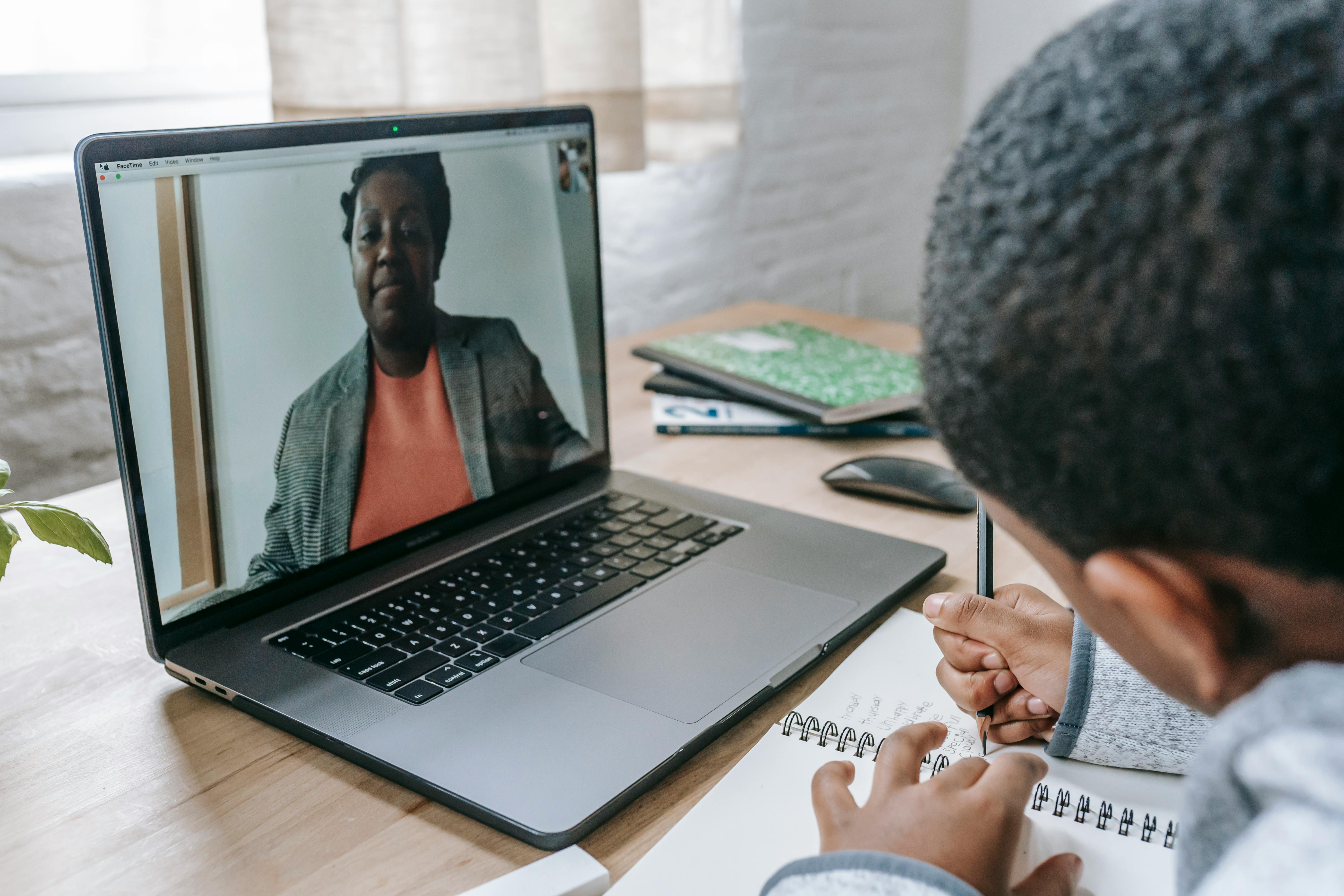 diligent black boy writing exam while teacher dictating online