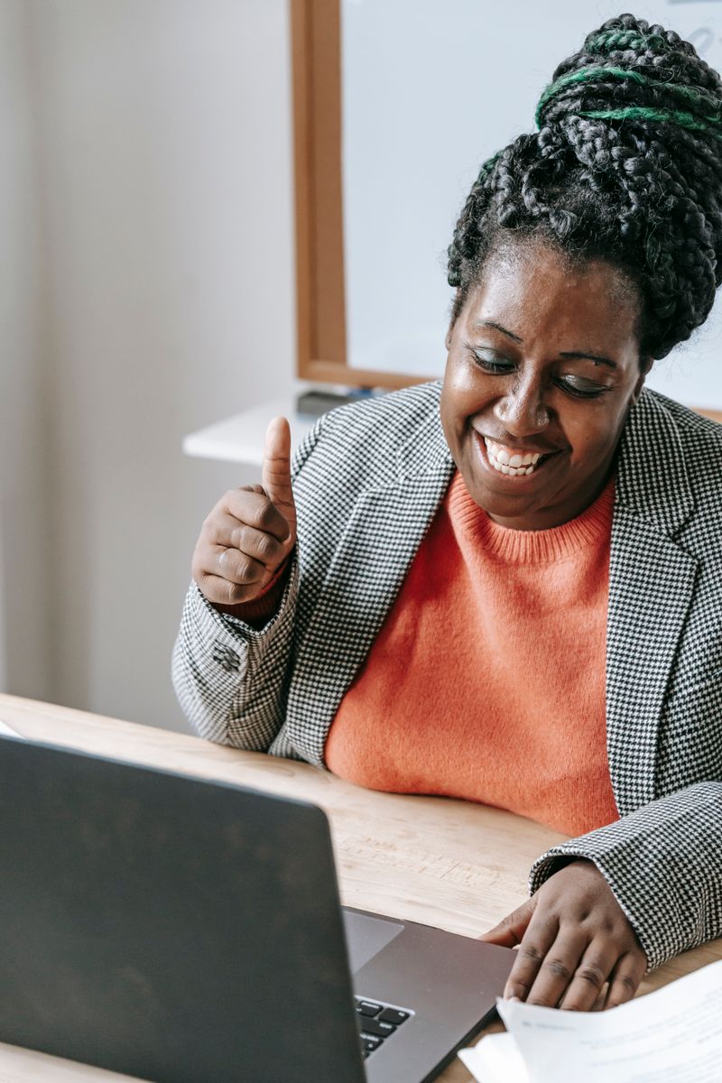 Black woman smiling and giving a thumbs up during a video call on a laptop, representing a positive virtual wellness consultation