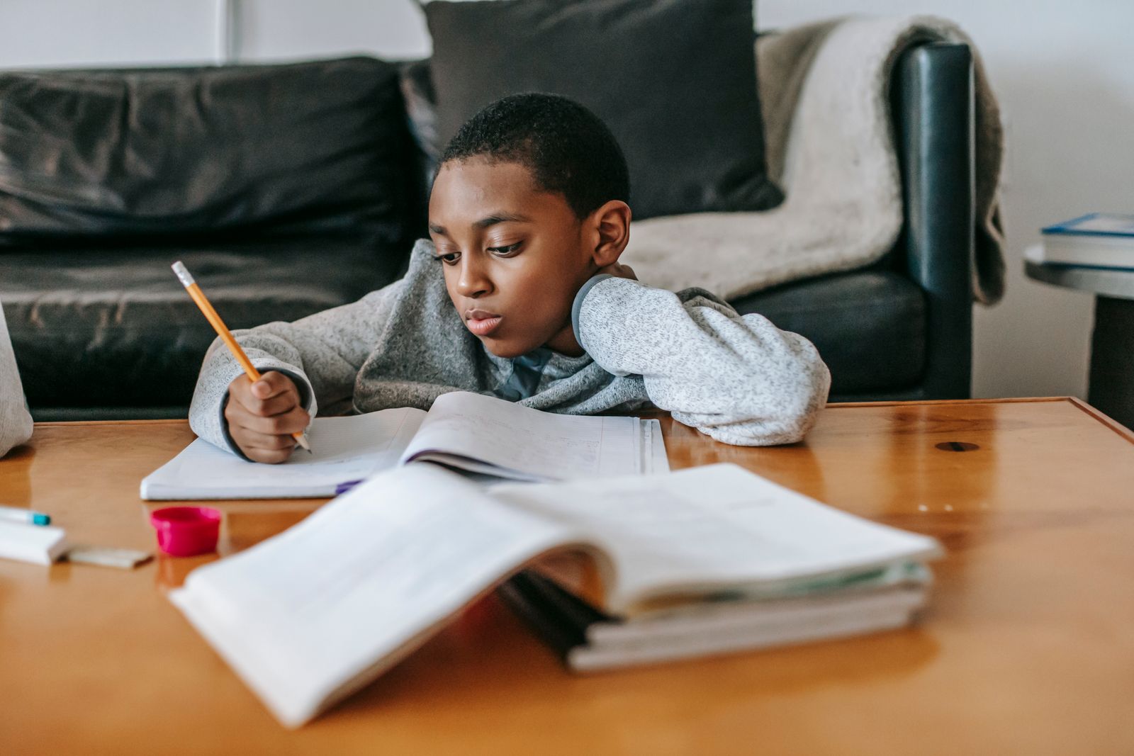 A young Black boy concentrating while writing in a notebook at a table at home, used to illustrate reporting on ADHD diagnosis and treatment gaps for Black children.