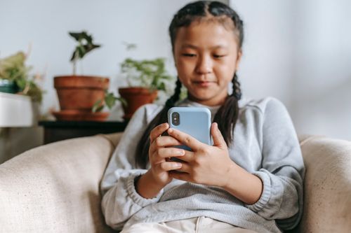 Free Focused Asian girl in casual clothes sitting on cozy armchair and browsing social media on smartphone Stock Photo