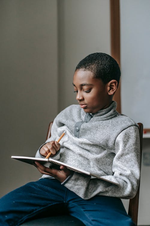 Focused black boy writing in notebook