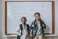 Focused multiracial children in casual outfits with backpacks standing in classroom against whiteboard at school and looking at camera
