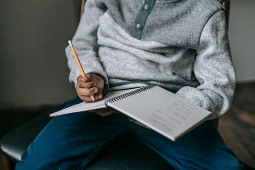 Free Crop unrecognizable African American pupil in casual clothes sitting on chair and writing in copybook while doing tasks Stock Photo