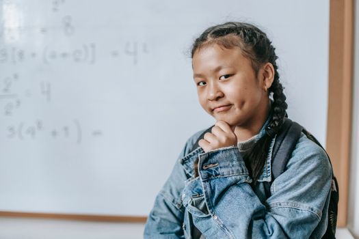 一位体贴的青少年学生身穿牛仔夹克，自信地在教室的白板前摆姿势