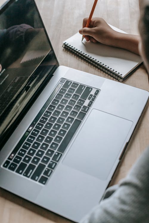 Free From above of crop anonymous female sitting at table with opened laptop and taking notes Stock Photo