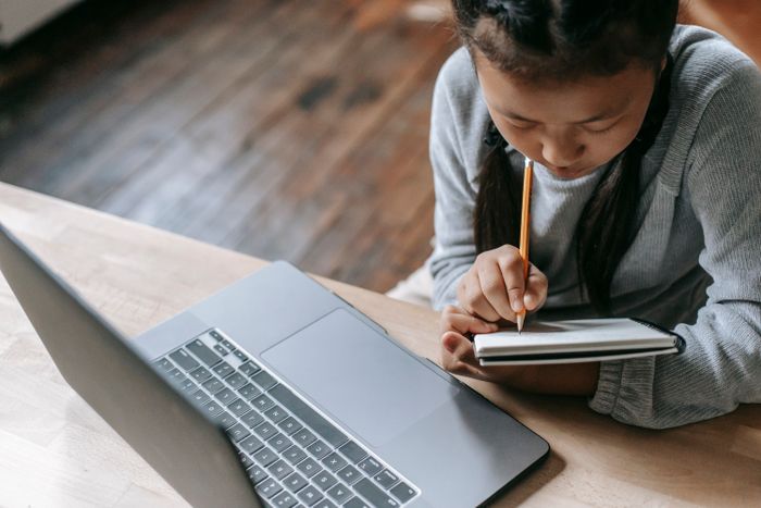 Student writing in a notebook beside a laptop