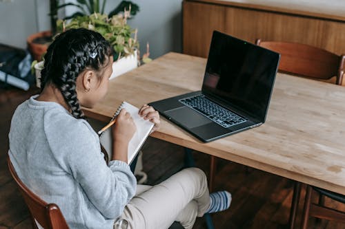 Free Ethnic girl writing notes studying with laptop Stock Photo