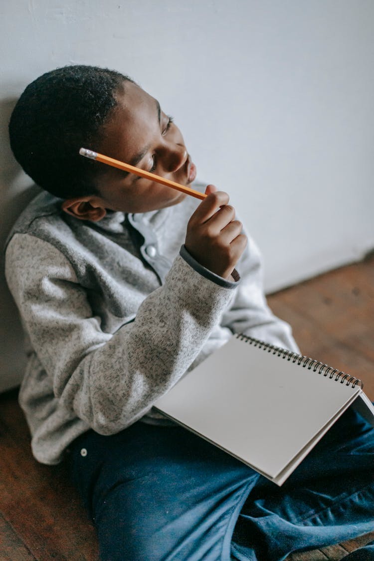 Pensive Black Kid With Notepad And Pencil