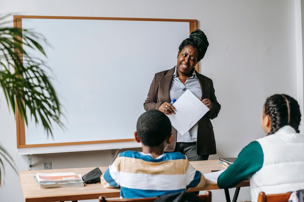 A teacher smiling warmly as she guides two pupils at their desk