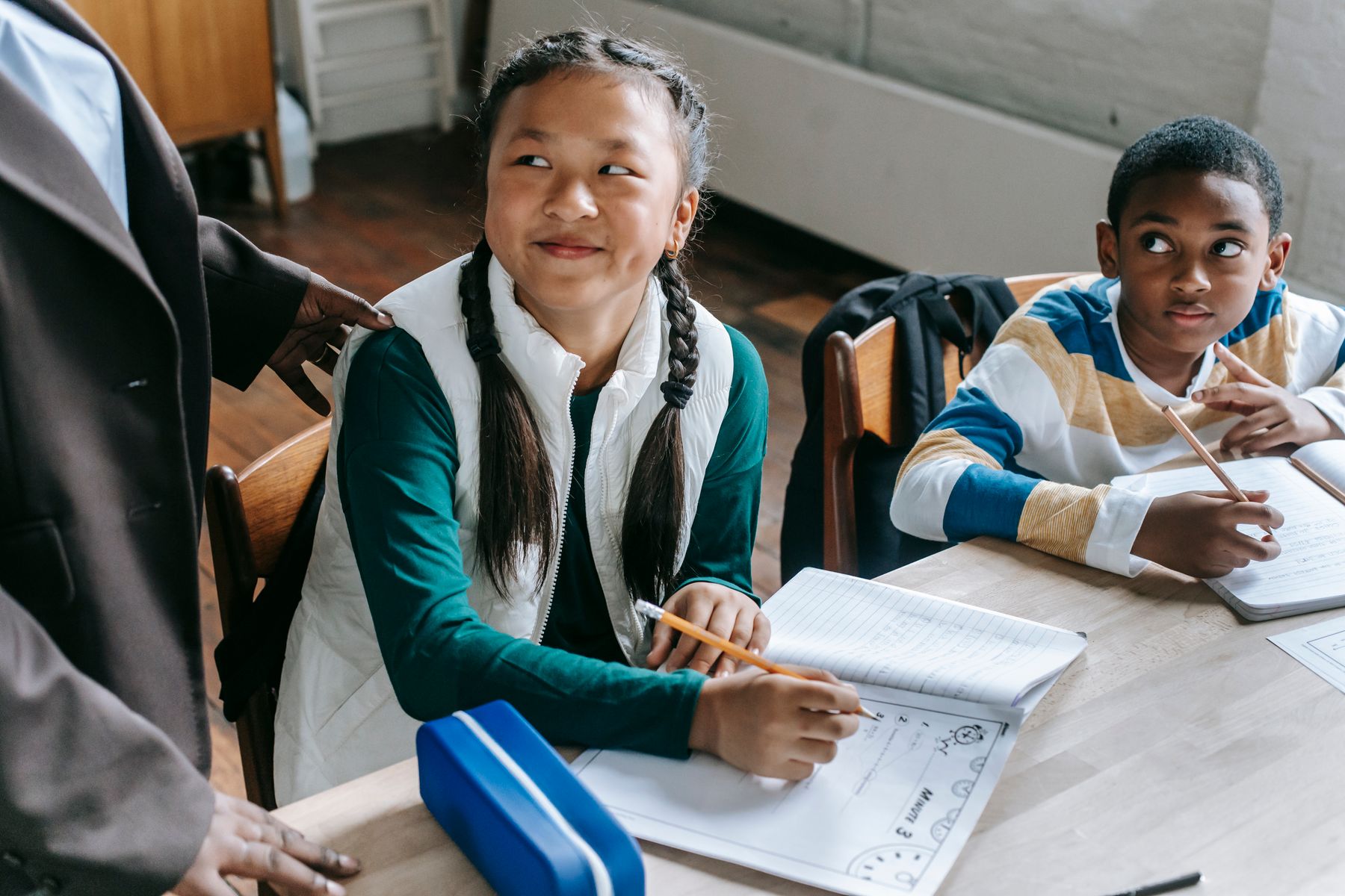 An educator working with two elementary-age students at a classroom desk