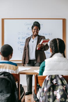 Back view of focused kids sitting at desk in classroom and listening to African American teacher against whiteboard