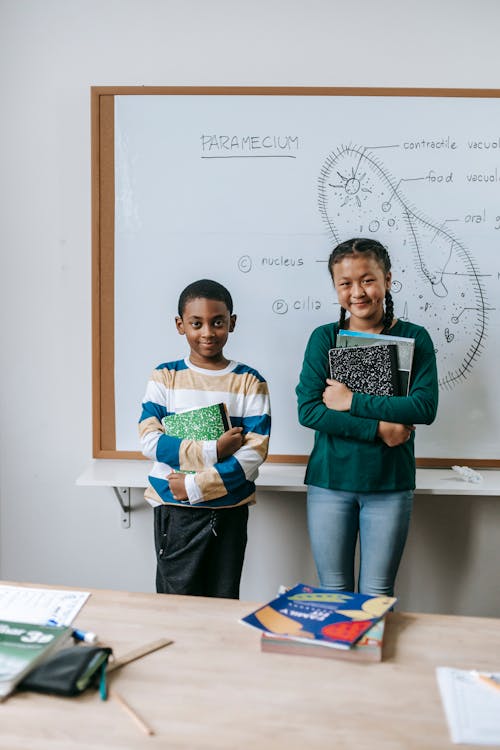 Cheerful multiracial schoolkids with notepads at whiteboard